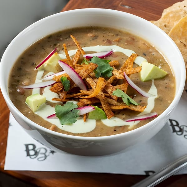 A bowl of Bar Bacoa's tortilla soup with avocado, radishes, cilantro, and tortilla strips.