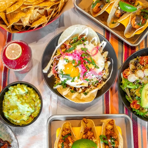 Overhead view of Bar Bacoa tacos, guacamole, chips, salad, and a red margarita on a striped tablecloth.