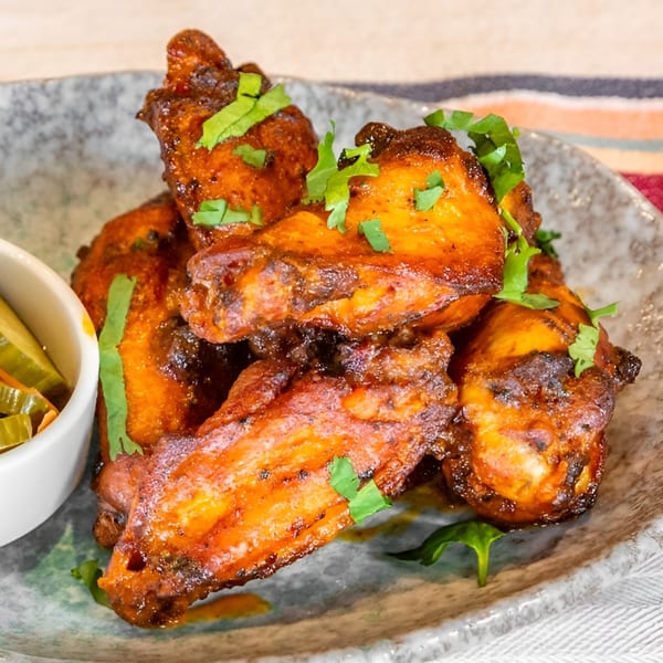 Close-up of Bar Bacoa's crispy, glazed chicken wings topped with fresh cilantro, served with pickled vegetables.