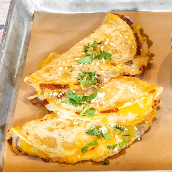 Three Bar Bacoa tacos with melted cheese, cilantro, and cotija cheese on a metal tray.