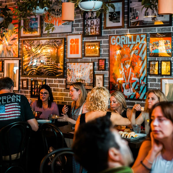 Patrons enjoying tacos and drinks at Bar Bacoa, with a brick wall adorned with framed art.