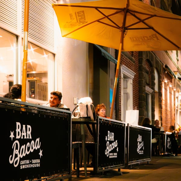 Bar Bacoa's outdoor patio at night, with patrons seated under a large yellow umbrella.