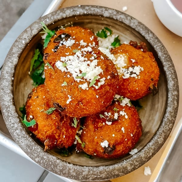 A bowl of golden-brown Bar Bacoa fritters topped with crumbled white cheese and fresh herbs.